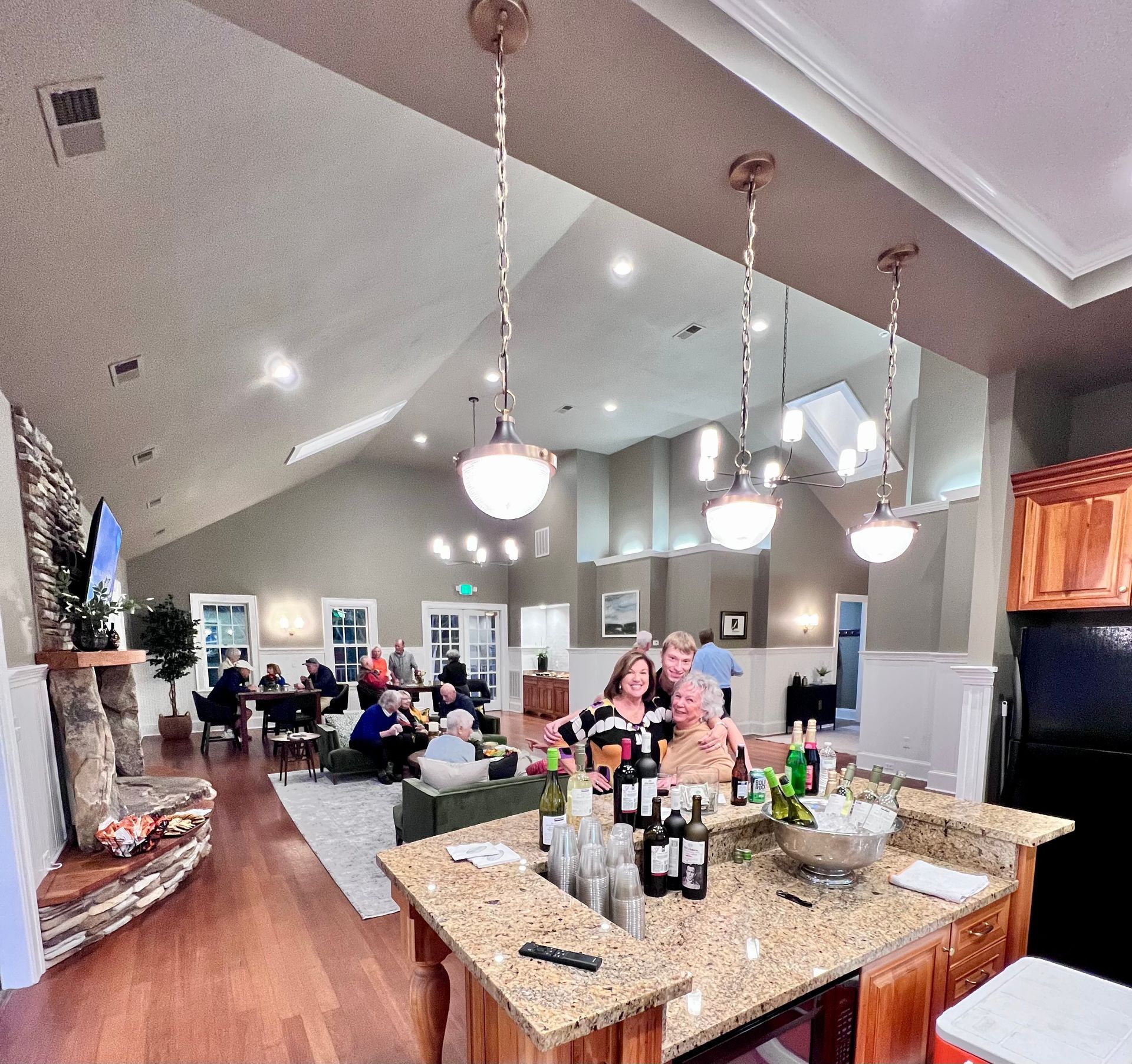 Bright kitchen and living room with people socializing around a granite island and nearby seating area