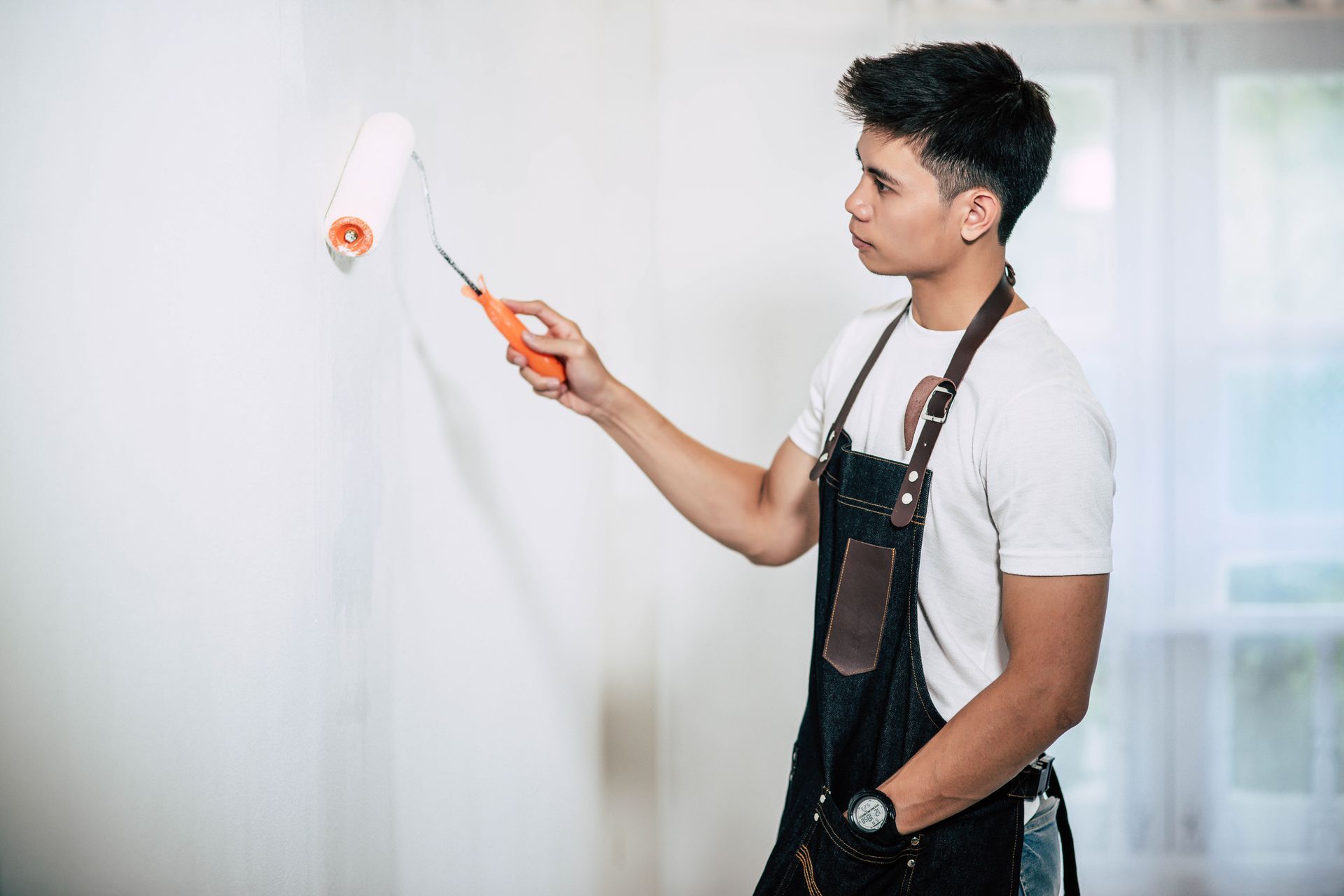 A man is painting a wall with a paint roller.