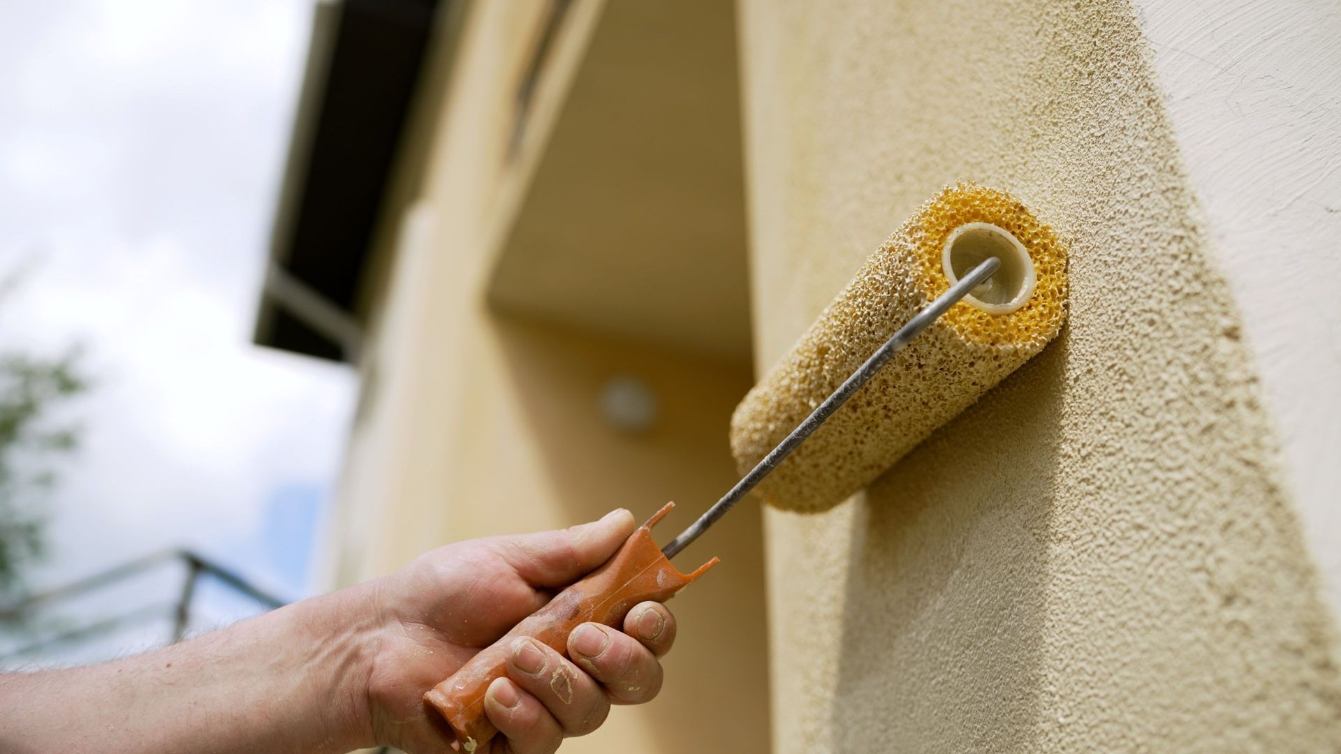 A man is painting the side of a building with a roller.