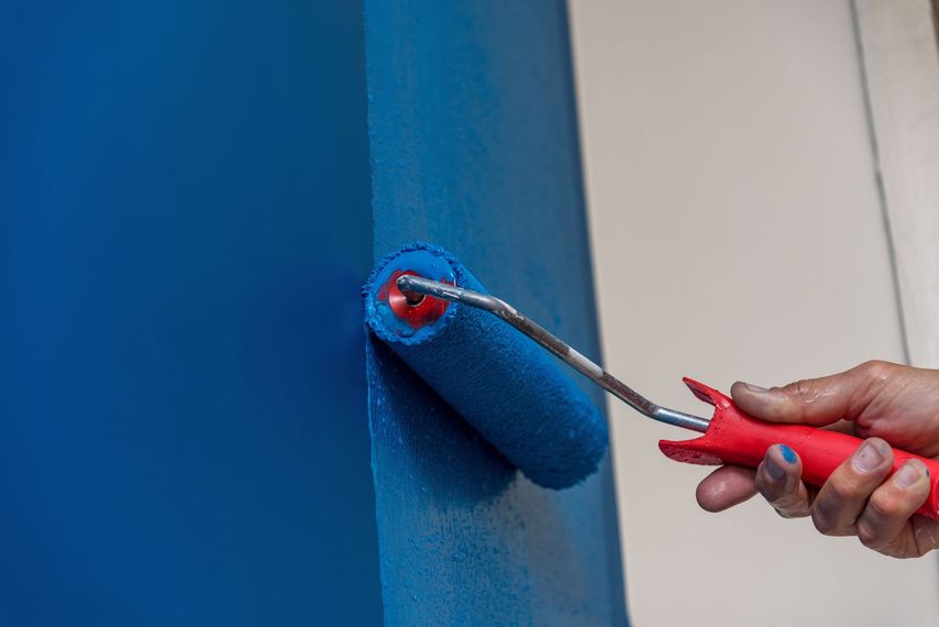A person is painting a wall with a blue paint roller.