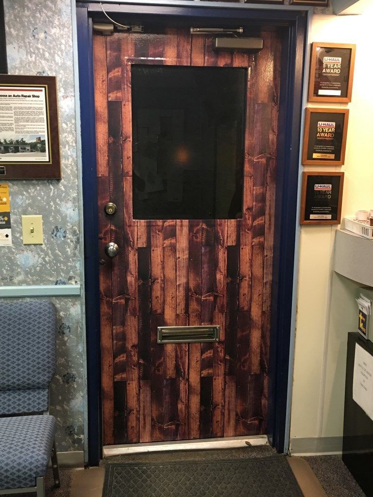 Rustic wooden door with a black window panel, set in a hallway beside wall plaques and posters