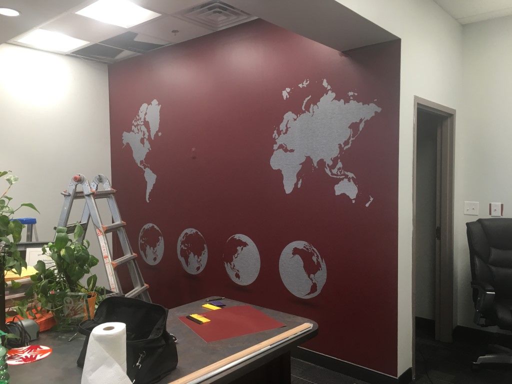 Office wall with maroon world map mural, ladder, plants, and desk in the foreground