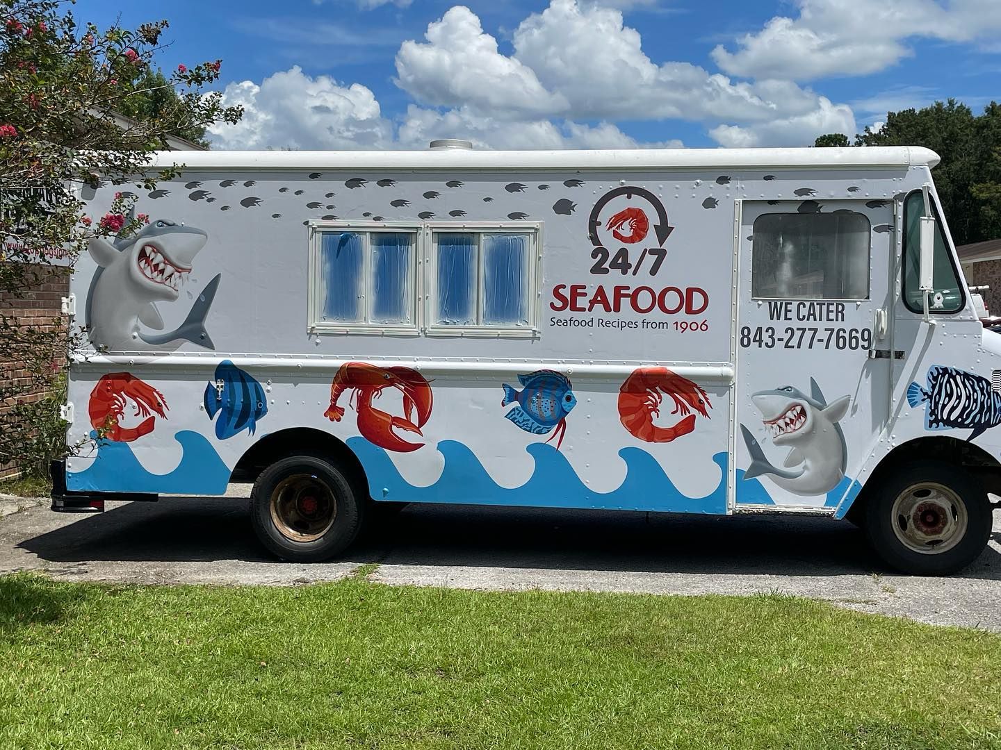 White seafood truck with blue wave and red crab graphics parked on grass under a cloudy sky