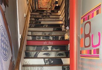 Staircase with decorated steps and wall art, leading up into a narrow indoor hallway