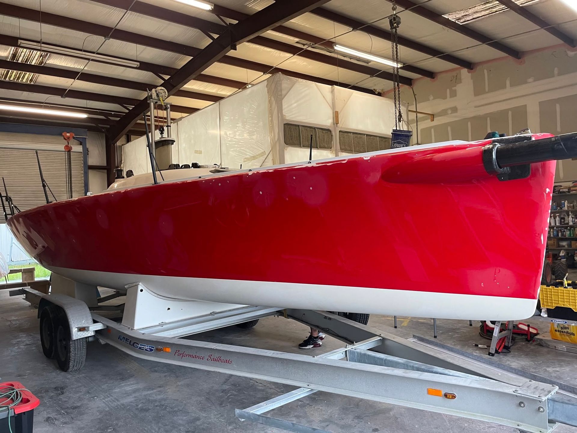 Red sailboat on a trailer inside a warehouse, with a white cover over the cockpit.