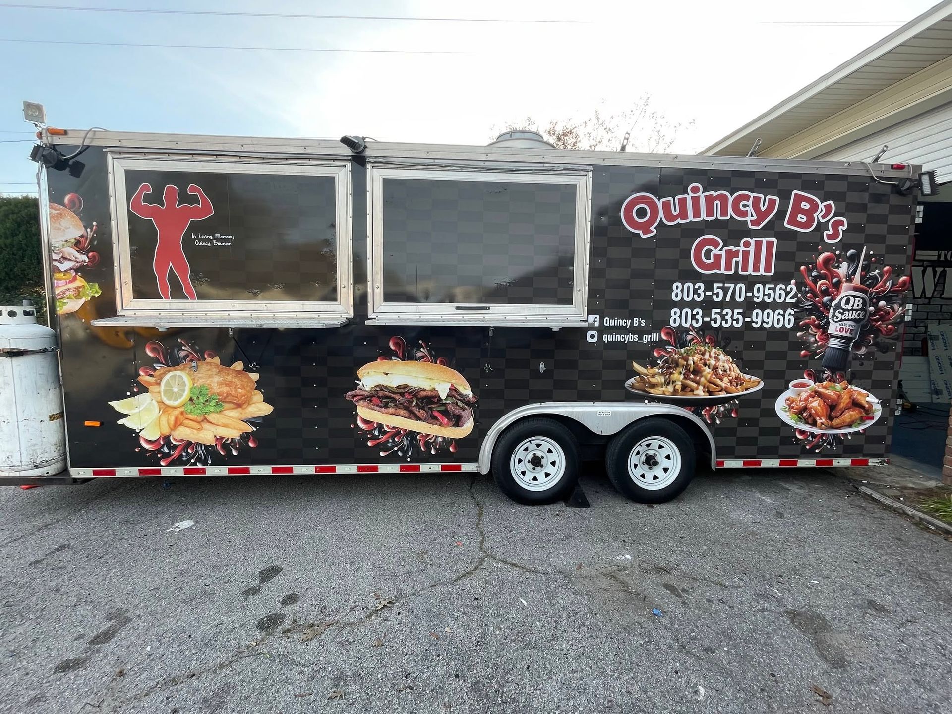 Food trailer with “Quincy Bz Grill” signage, window, and burger images parked by the roadside