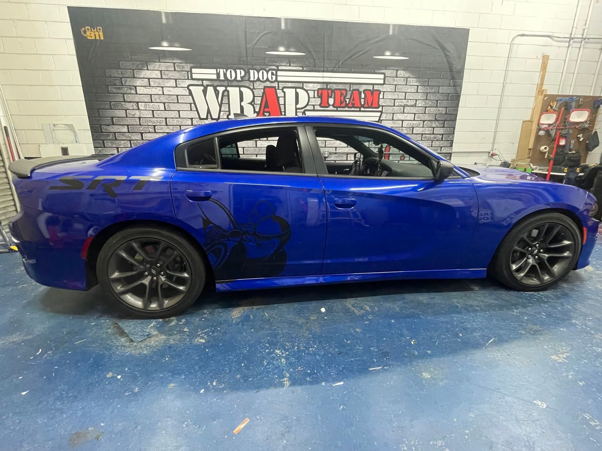 Blue sports coupe in a shop with a WRAPTRIX wall sign and blue floor covering