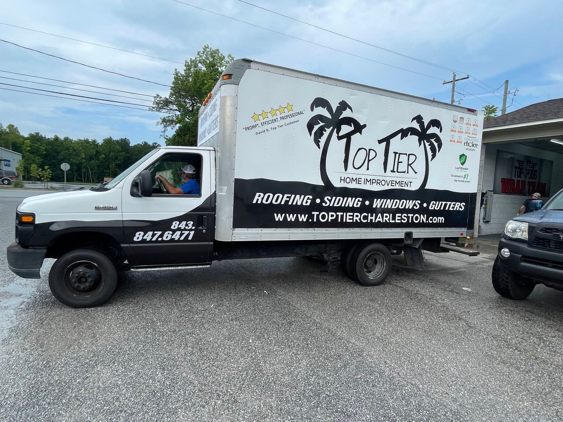White roofing company box truck with palm tree logo parked on gravel lot under cloudy sky