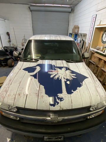 White SUV with blue hood graphic parked in a garage, front view.
