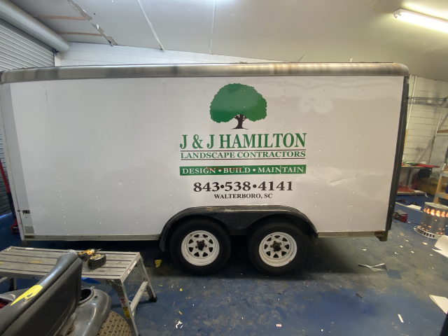 White J&J Hamilton trailer with green logo parked indoors in a garage-like space