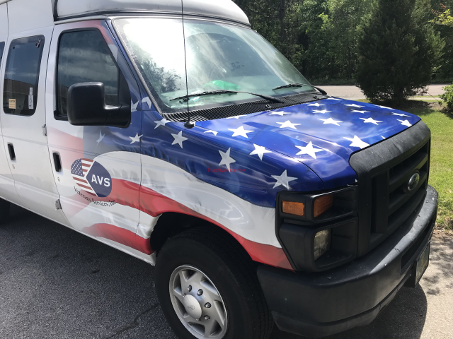 White van with an American flag wrap parked on a street, front-left view