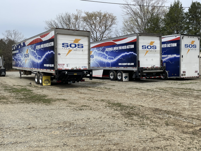 Three white SOS moving trucks parked in a gravel lot, seen from behind and side.