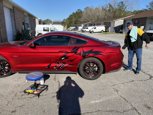 Red sports car with black flame decals, a small stool in front, and a person standing beside it in a parking lot.