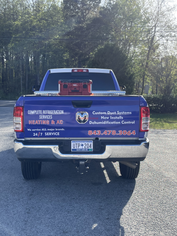 Blue pickup truck with a business sign on the tailgate, parked on a road near trees.