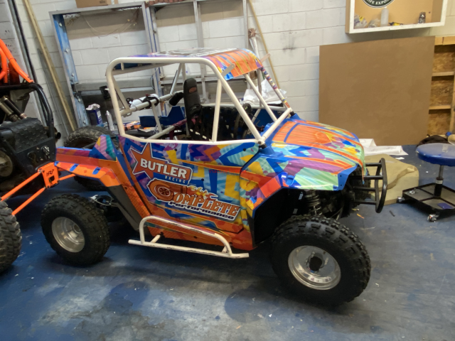 Colorful off-road dune buggy with orange, blue, and pink graphics parked indoors in a garage.