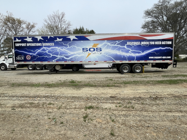 Blue emergency response trailer with lightning graphics and “SOS” text parked outdoors on grass