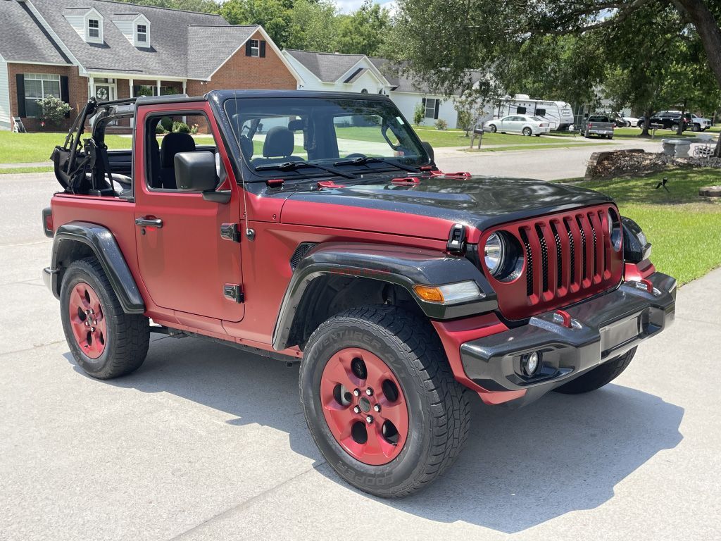 Red Jeep Wrangler with doors off parked on a suburban street in daylight