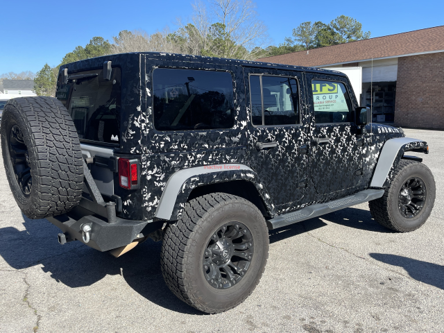Black Jeep Wrangler with camouflage pattern parked outside on a sunny day.