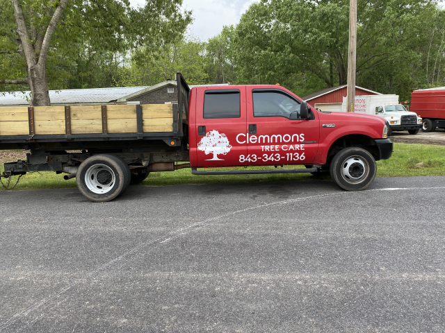 Red Clemons landscaping truck with flatbed trailer parked beside a road