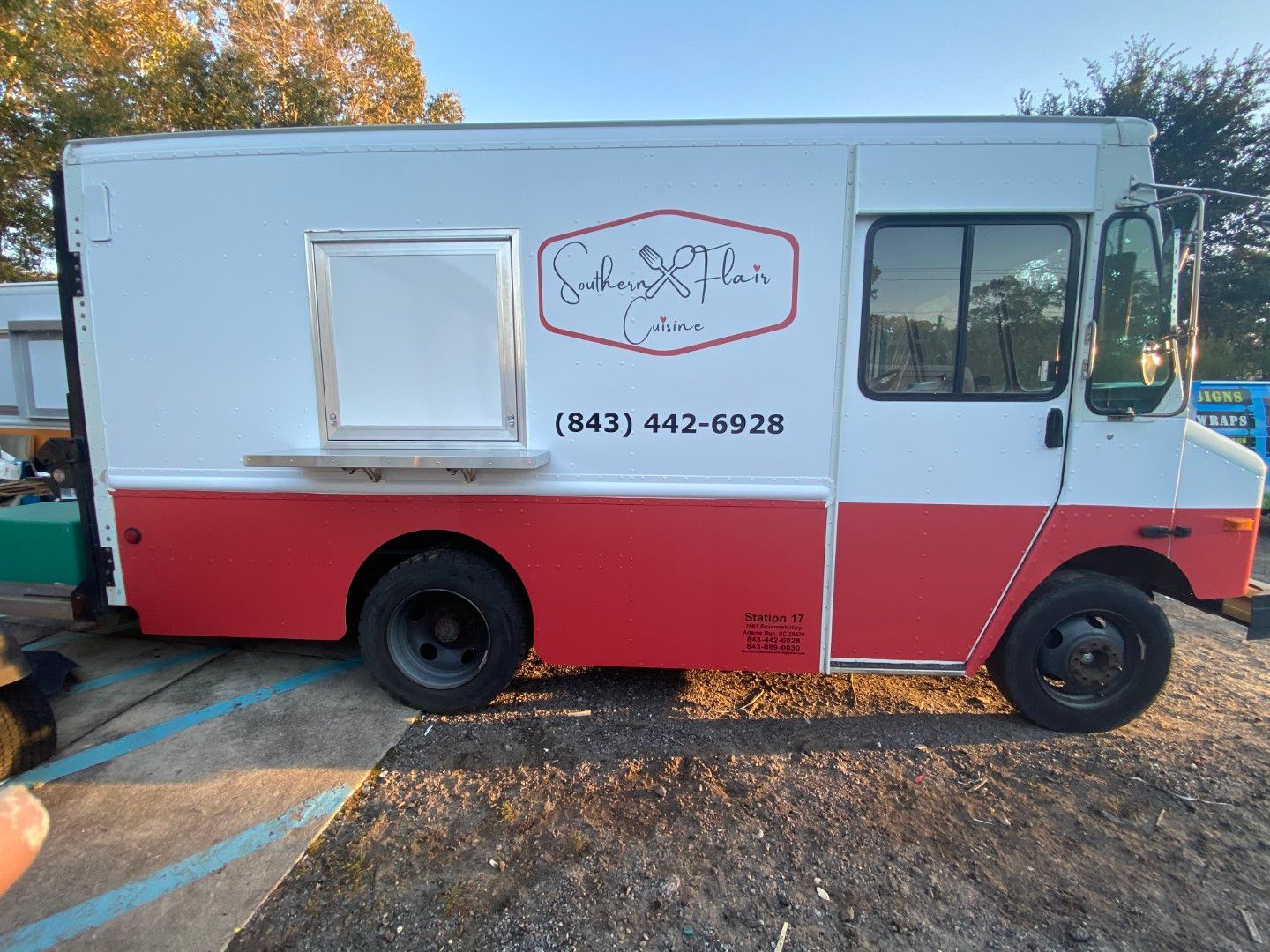 White and red food truck parked outdoors with a service window and phone number on the side