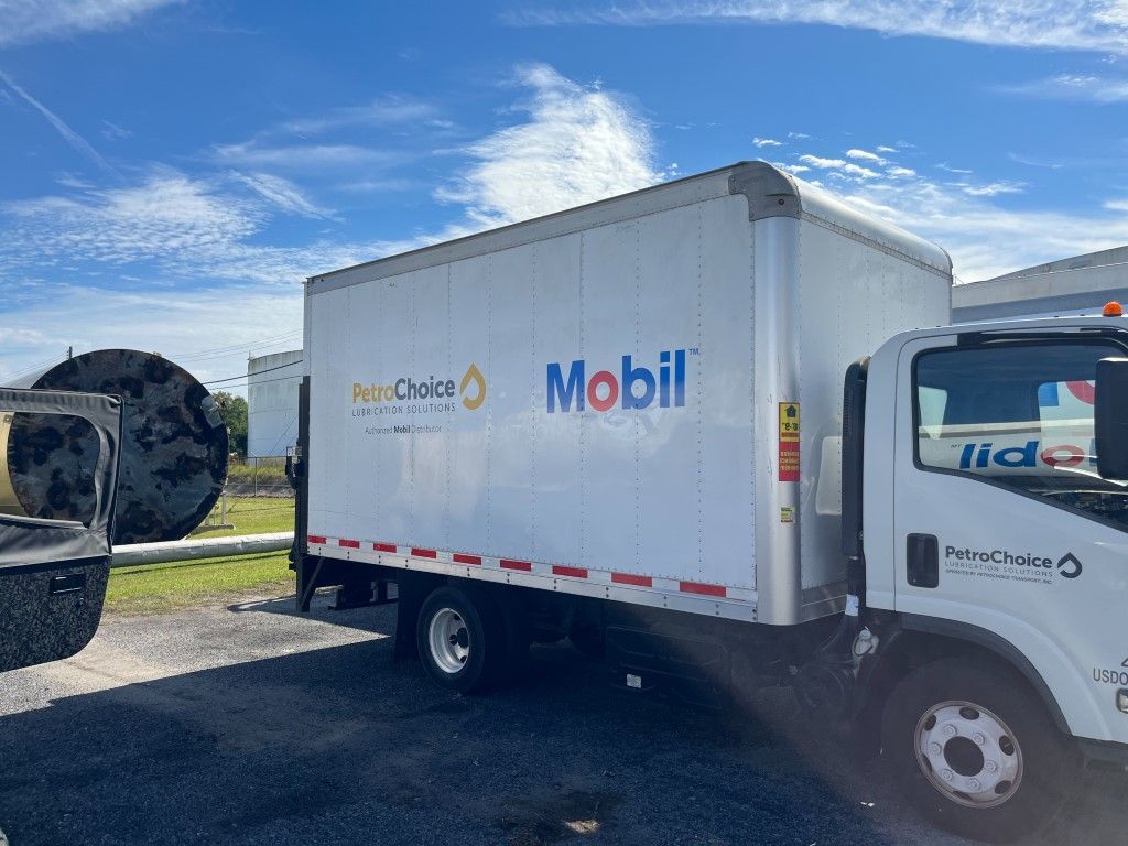 White Mobil-branded truck parked outdoors under a blue sky, with a large tire beside it.