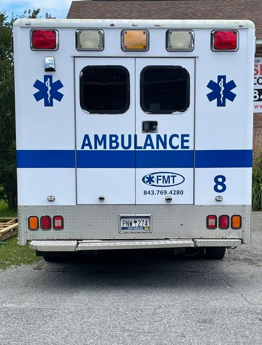 Rear view of a white ambulance with blue markings and red lights parked on pavement.