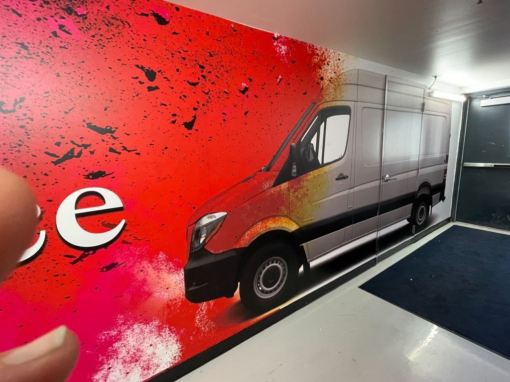 Gray van in a parking garage beside a red wall mural with partial white lettering