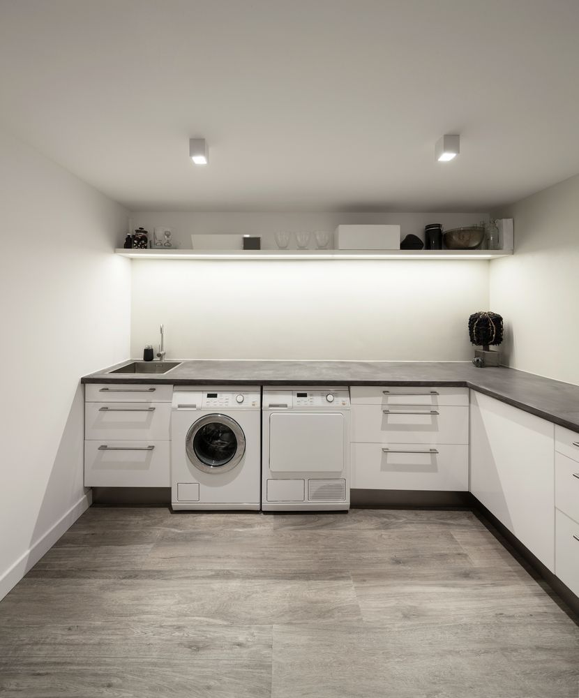 Laundry Room With White Cabinets, Dark Countertop, Washing Machine, Dryer, and Overhead Shelf — Payton Kitchens in Oakey, QLD