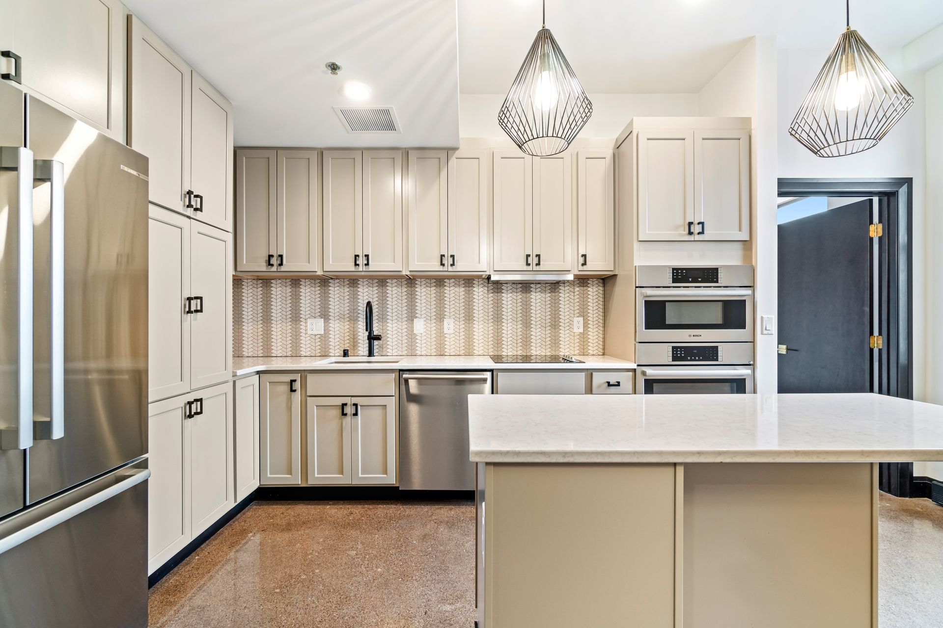Modern kitchen with light cabinets, stainless steel appliances, island, pendant lights, and light countertops.