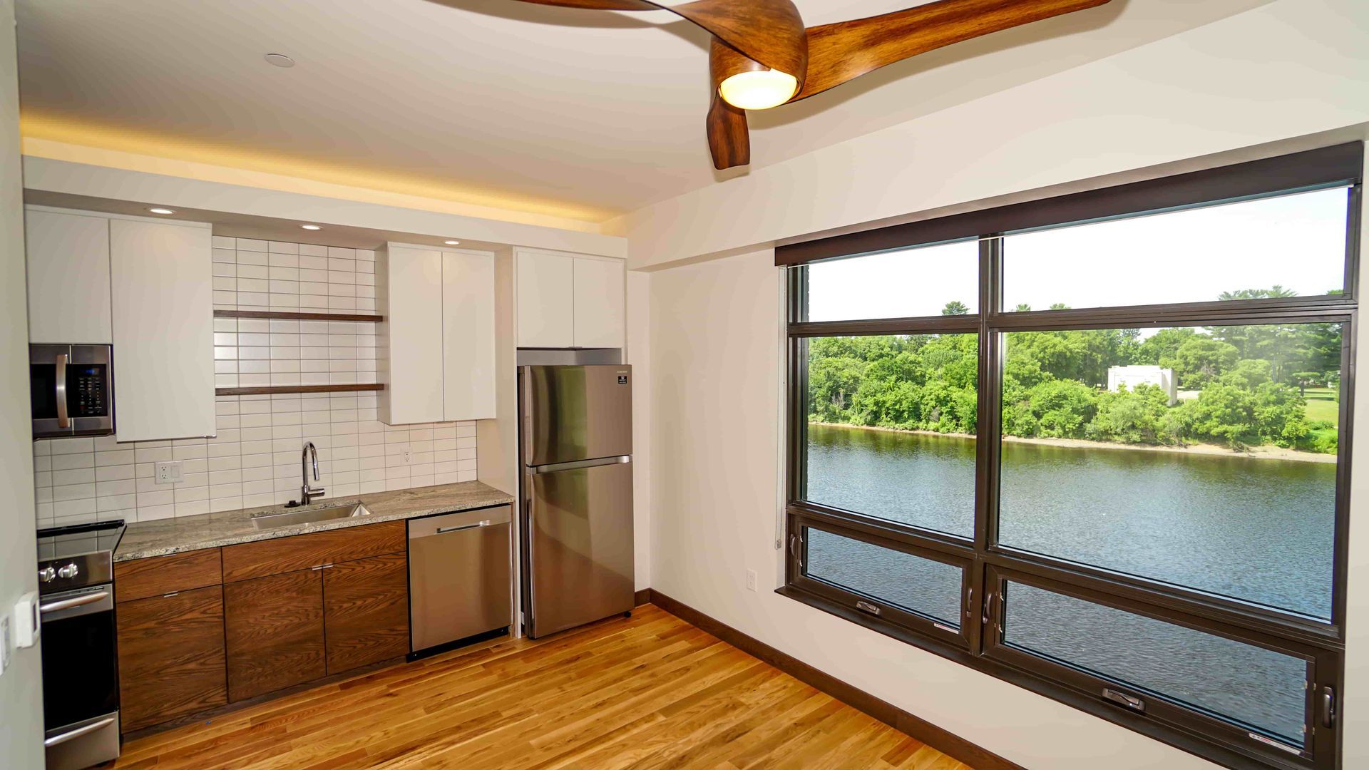 A kitchen with a ceiling fan and a large window overlooking a lake.