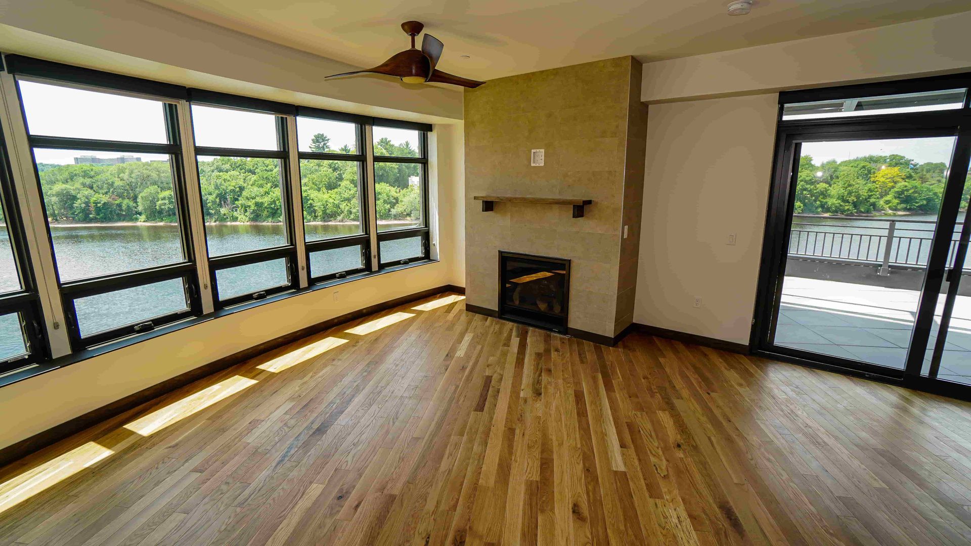 An empty living room with a fireplace and lots of windows overlooking a lake.