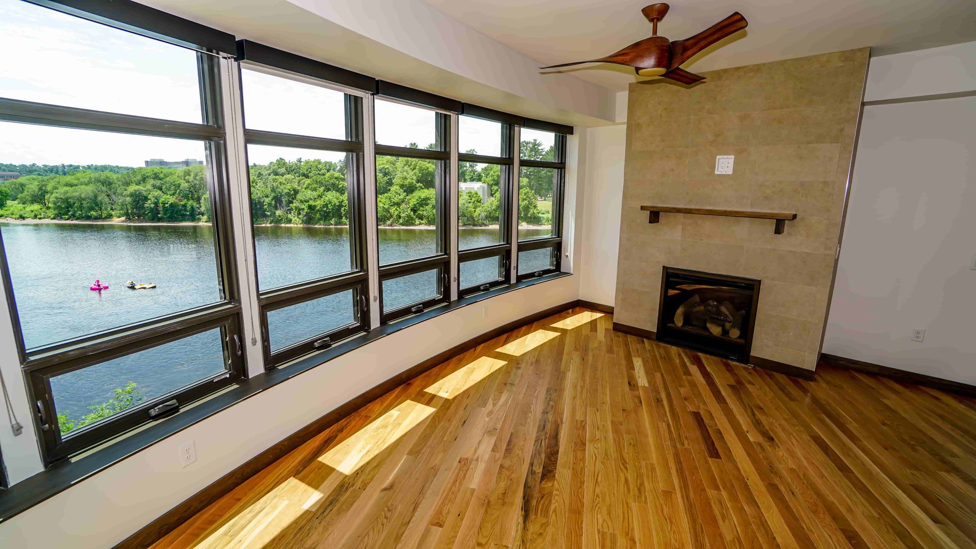 An empty living room with a fireplace and lots of windows overlooking a lake.