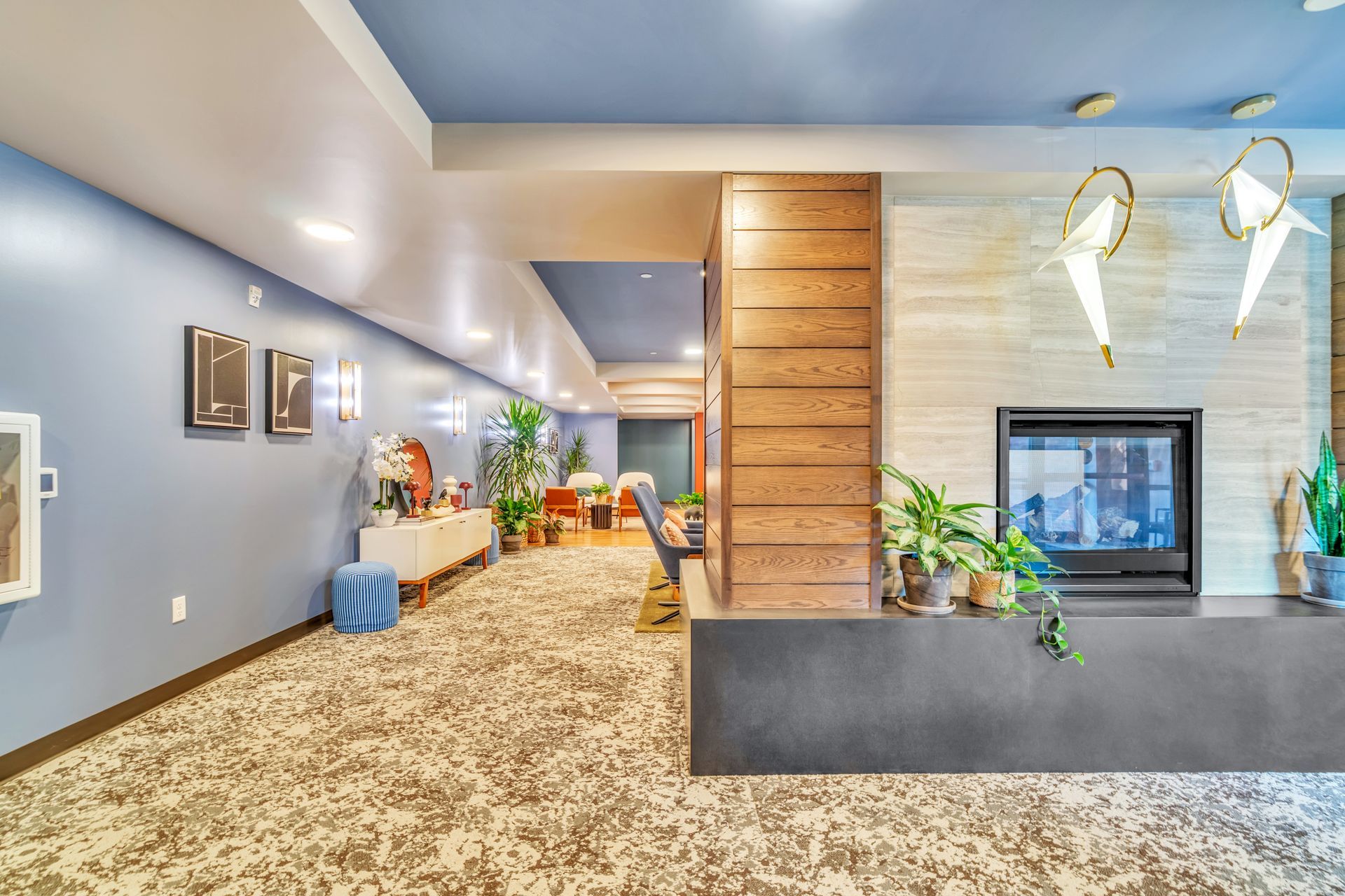 A hallway with blue walls, wood paneling, and a fireplace, carpeted floor, and plants.