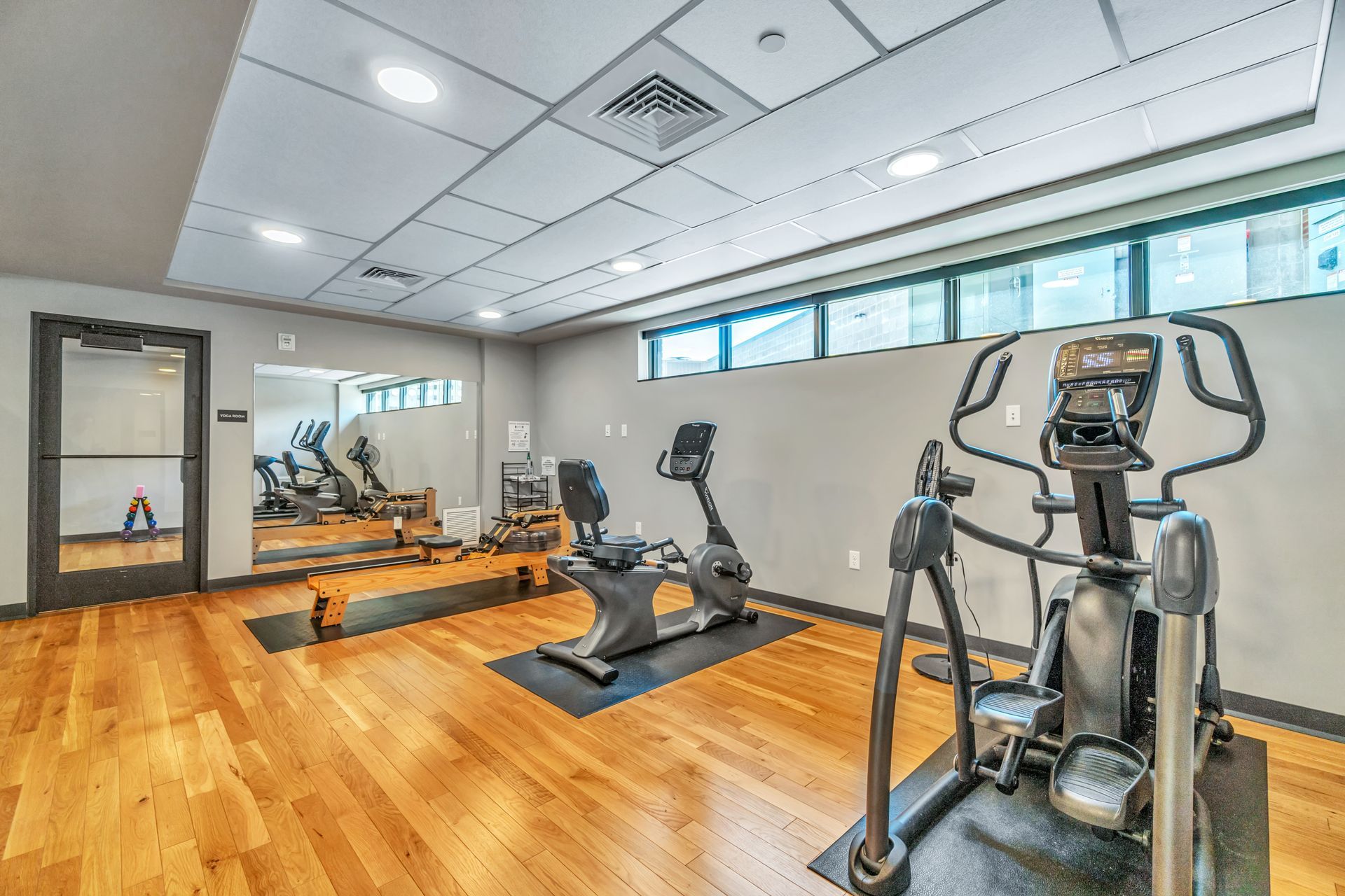 Small gym with exercise equipment, hardwood floors, and a mirror on the wall.