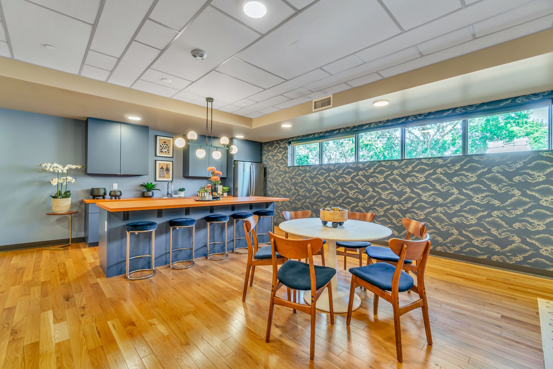 Modern kitchen with blue cabinets, wooden floors, island with stools, and dining table.