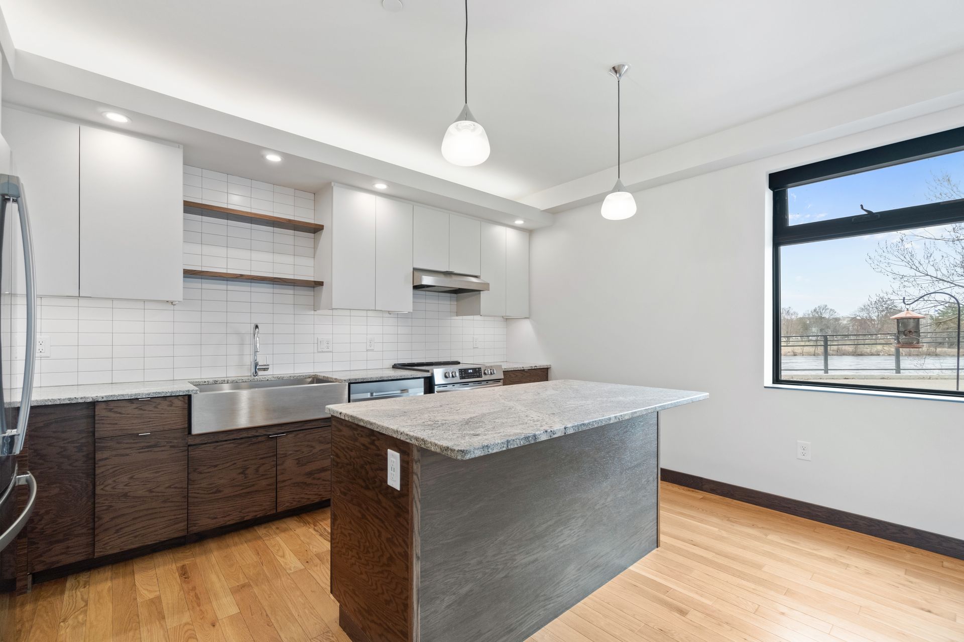Modern kitchen with gray and brown cabinets, stainless steel sink, island, and window.