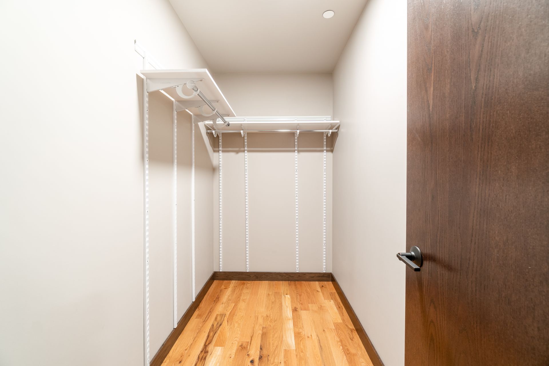 Small closet with light wood floor and brown door; white shelves and rods.