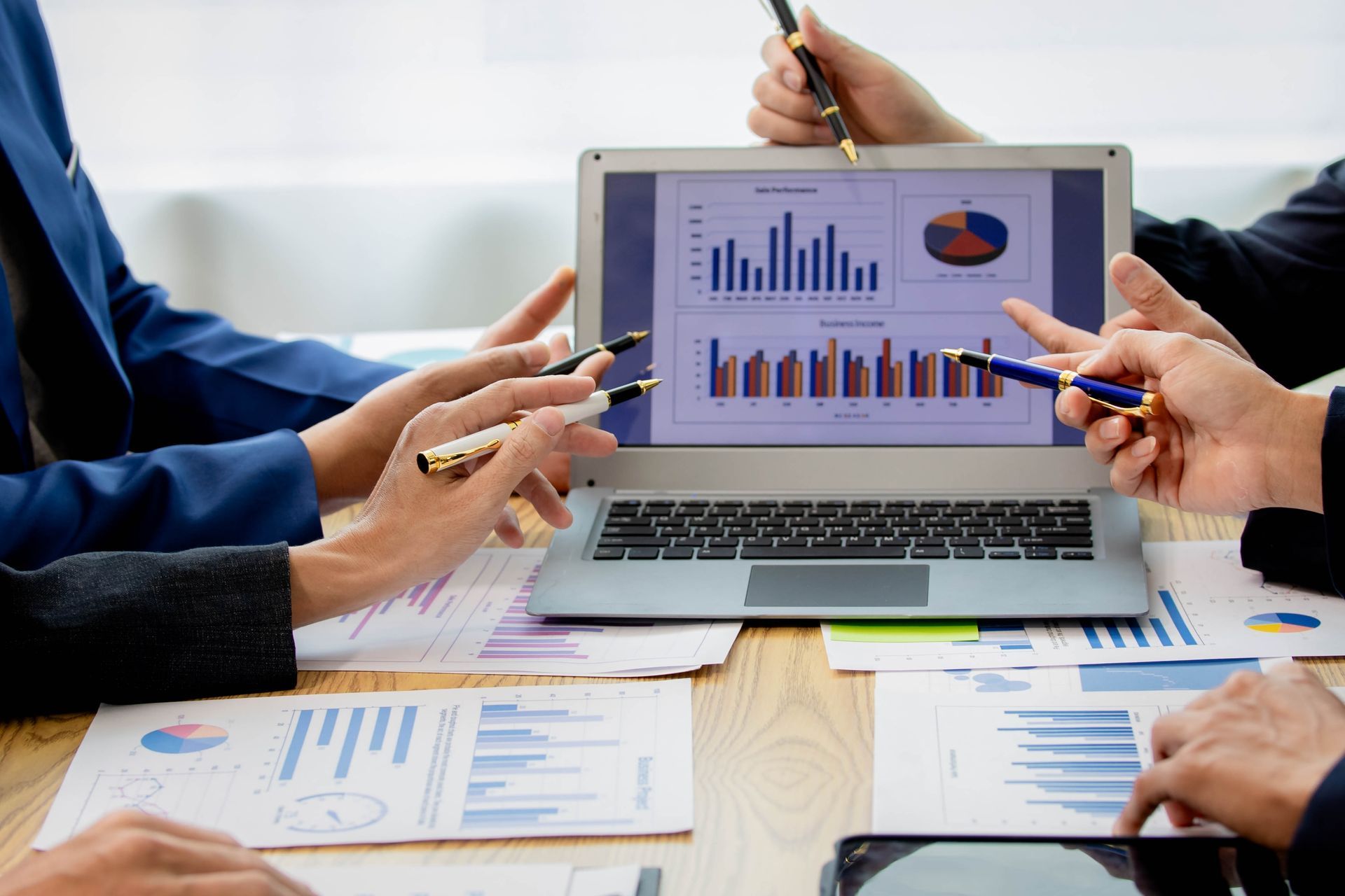 Hands pointing at a laptop displaying charts and graphs during a business meeting