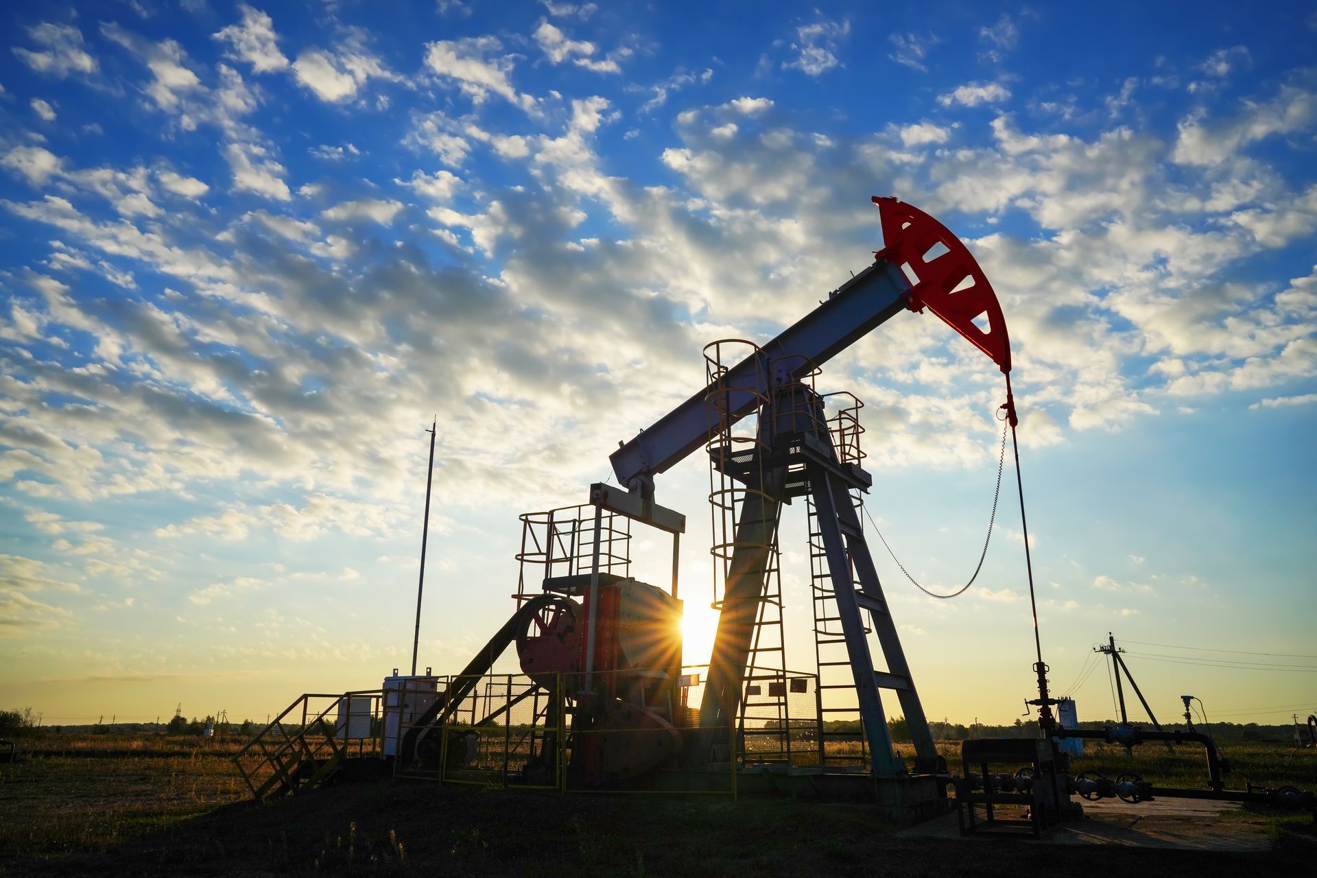 Oil pumpjack silhouetted at sunset under a cloudy sky.