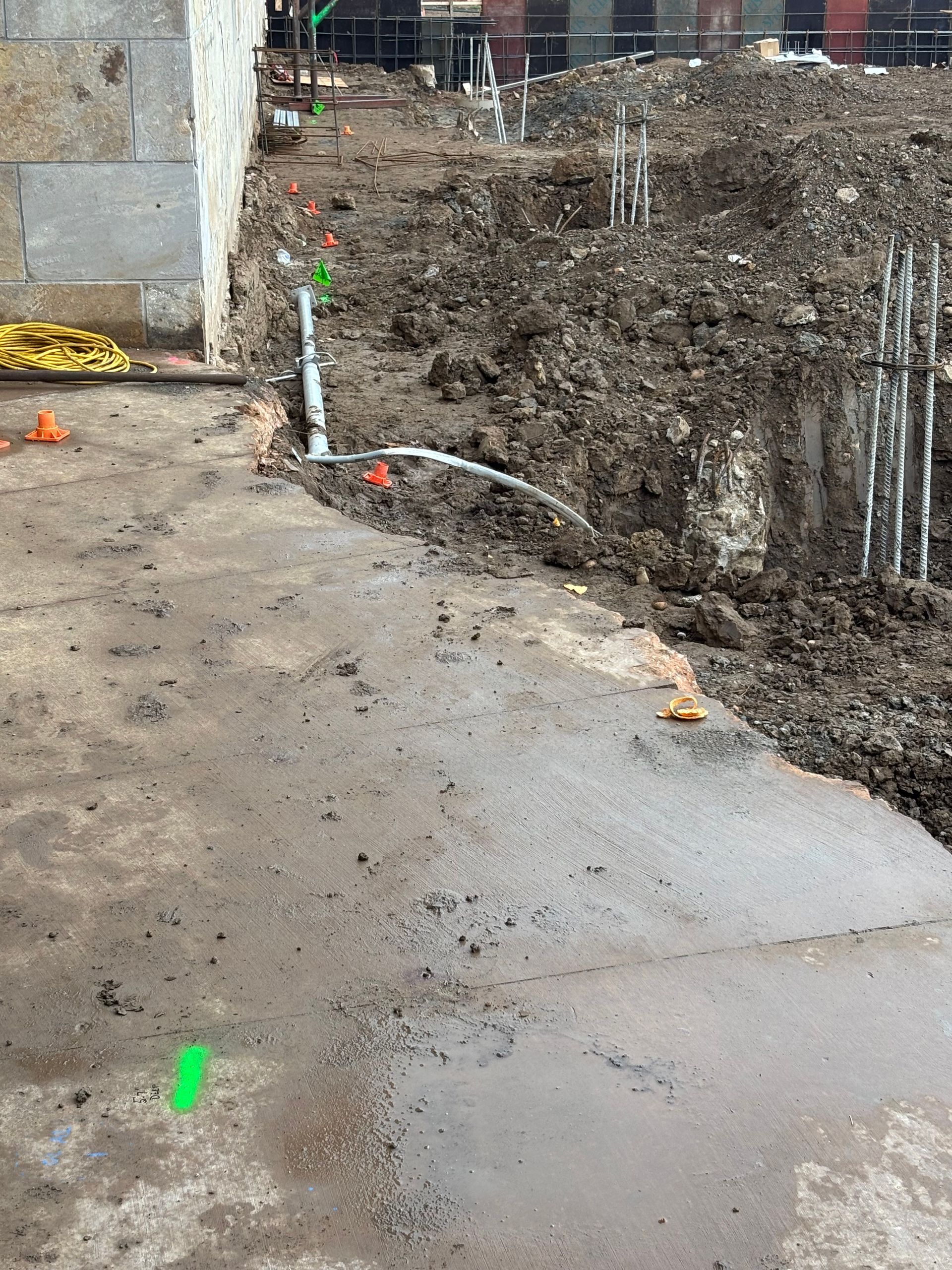 Construction site with muddy ground, concrete path, and exposed utilities.