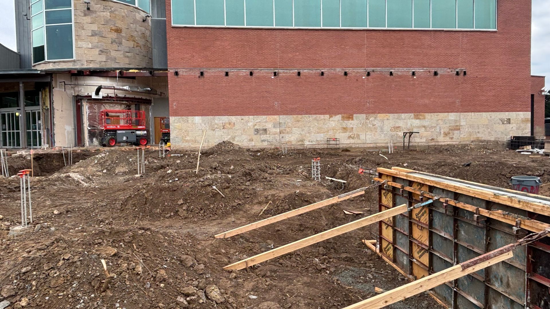 Construction site next to a brick building. Excavation with wood framing and a lift.