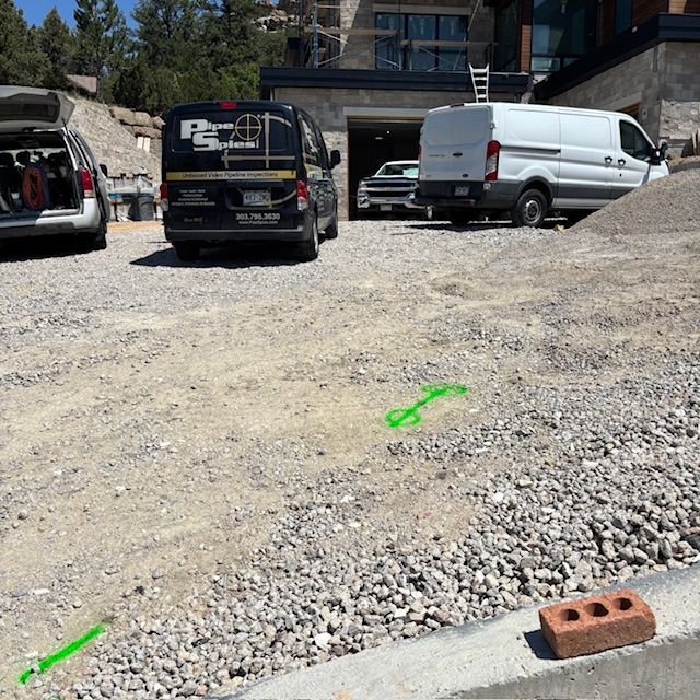 Construction site with gravel and vehicles. A brick sits on the curb. Green arrows mark the ground.