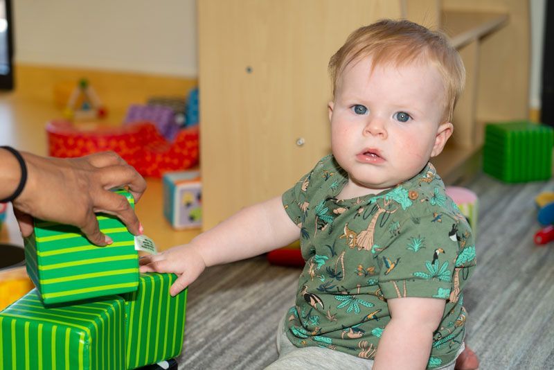 A baby is sitting on the floor playing with blocks in a classroom at Thornlie Early Learning Centre.