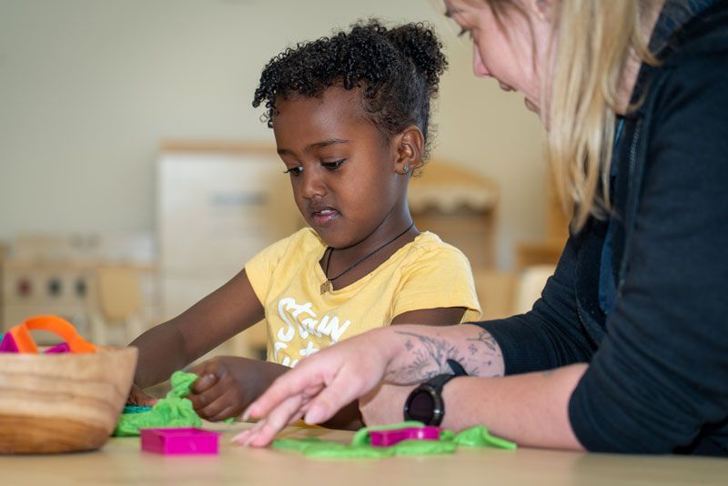 A childcare educator is playing with a little girl at a table at Thornlie Early Learning Centre.