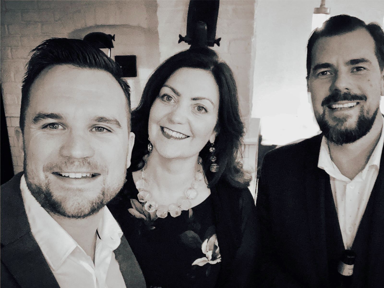 L-R: Alan Dixon, Liz Prince and Stig Strand smiling at the camera. Photo is in black and white.