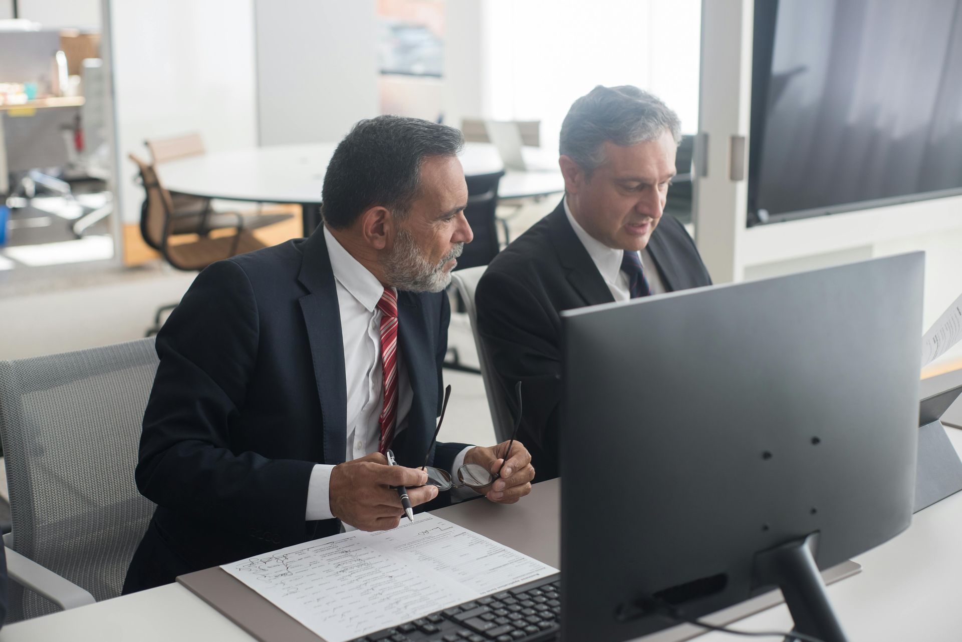 Two men are sitting at a desk looking at a computer screen.
