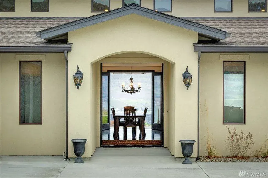 Beige house exterior with arched entryway to dining room, dark wood table, chandelier. Two urns flank the doorway.