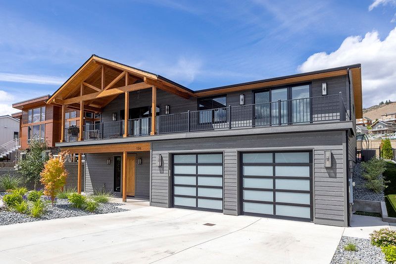 Modern two-story house with gray siding, two-car garage, and wooden accents. Blue sky.