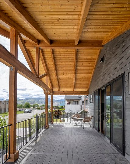 Covered wooden deck with railing, mountain view, gray siding and doors.