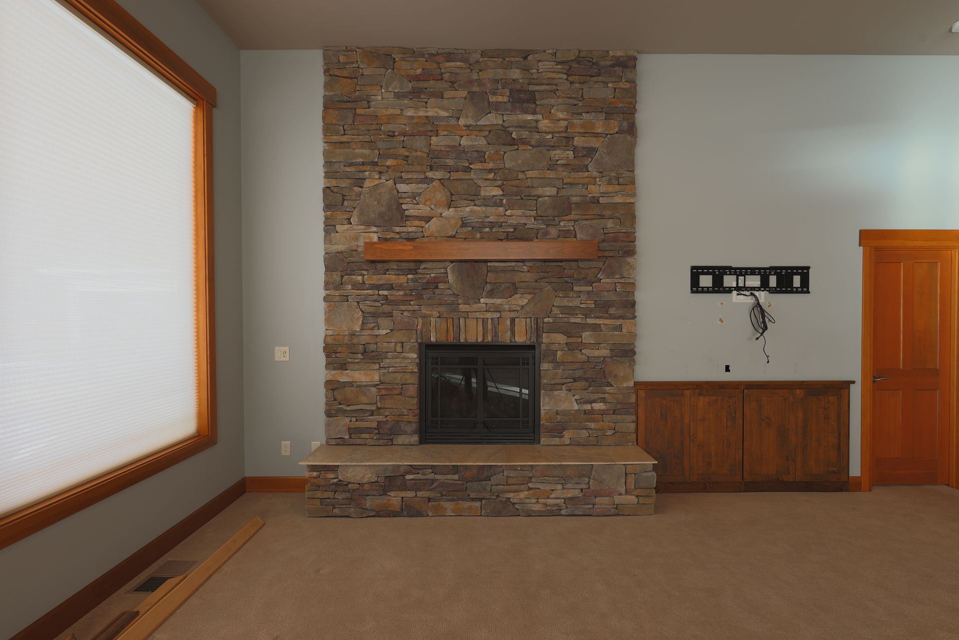 Stone fireplace with wooden mantle and matching wooden door in a room with light blue walls and a large window.